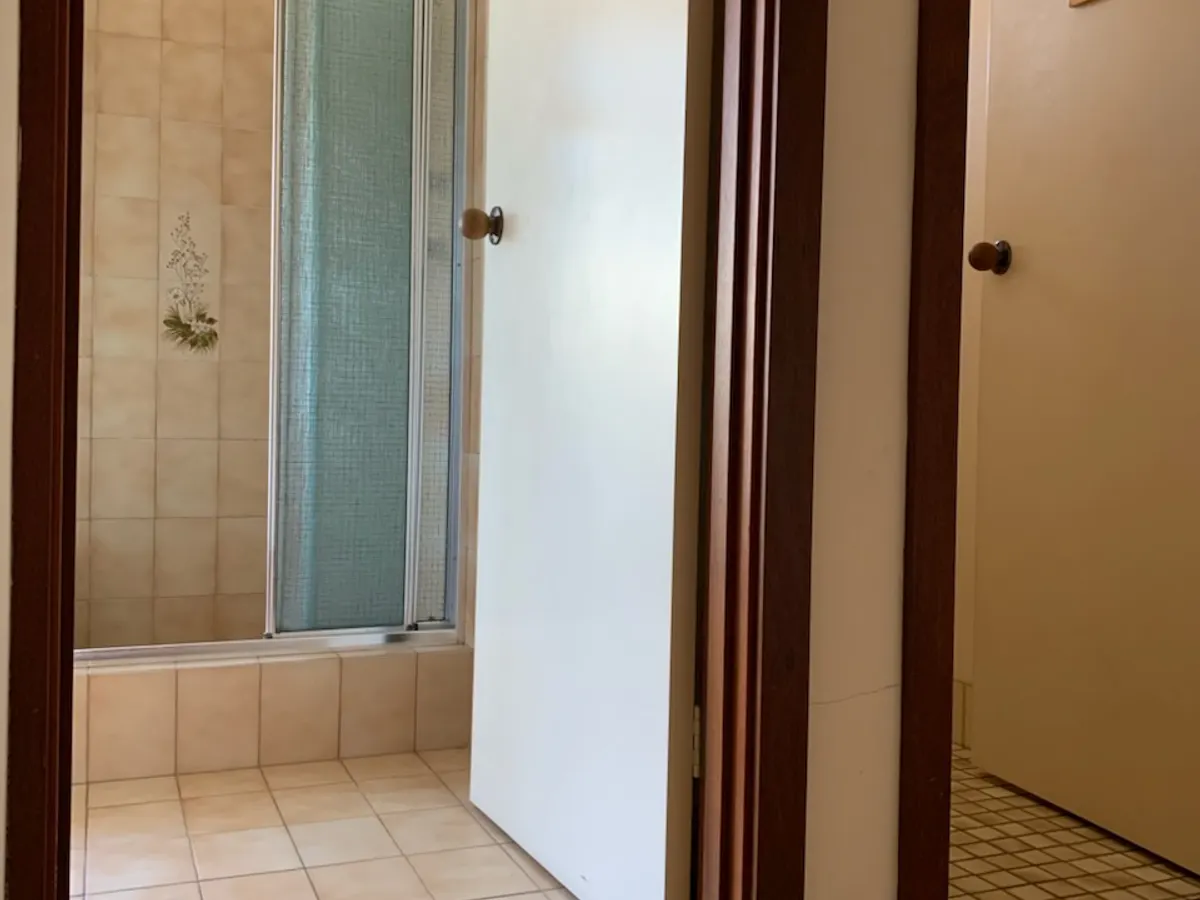 Before: the narrow doorway into the old Bull Creek bathroom, with a framed shower screen on a tiled hob