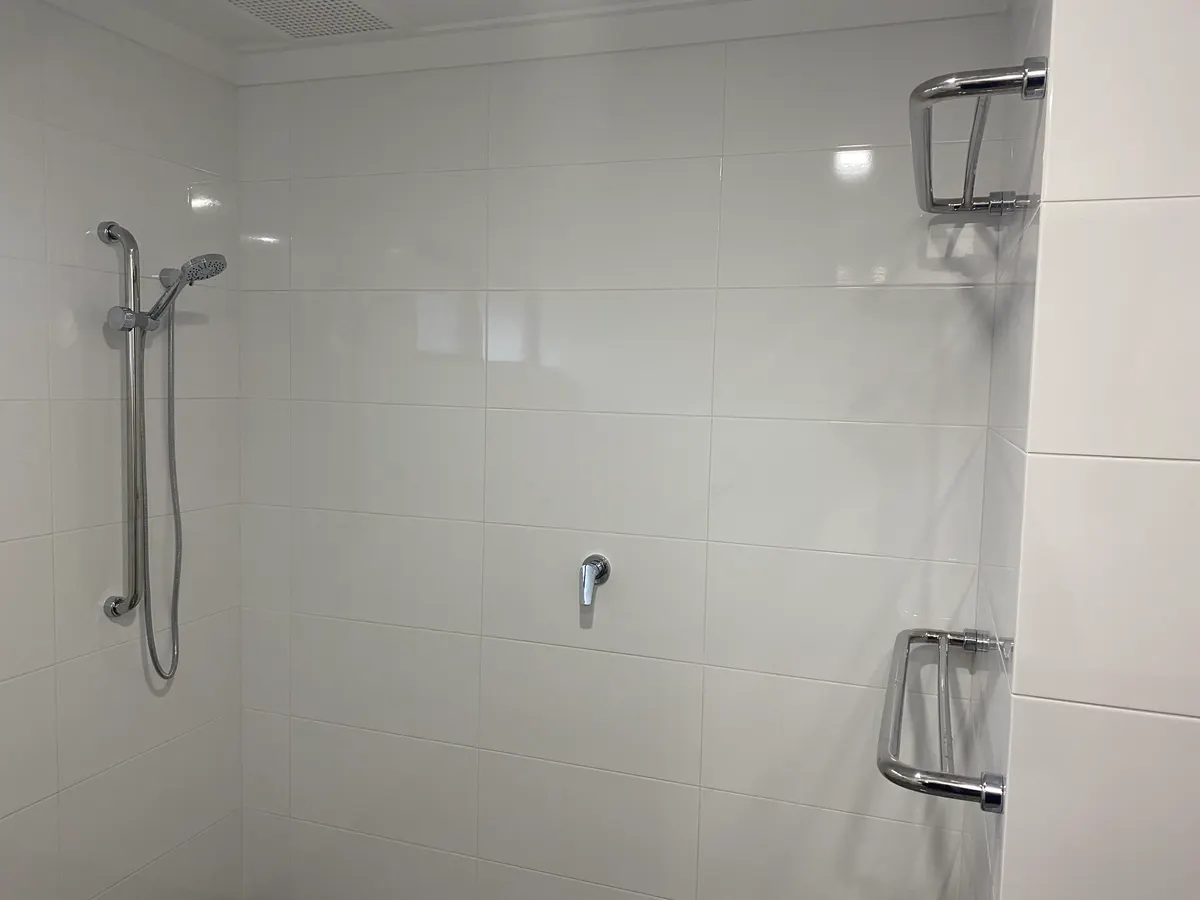After: the level shower area with a hand shower on a rail and fold-up grab rails, tiled to ceiling height
