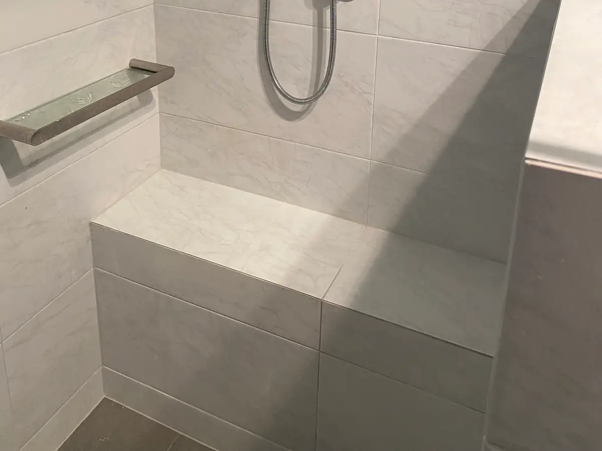 After: a large tiled built-in seat at the end of the Midland shower, with a hand shower on a rail and a towel rail