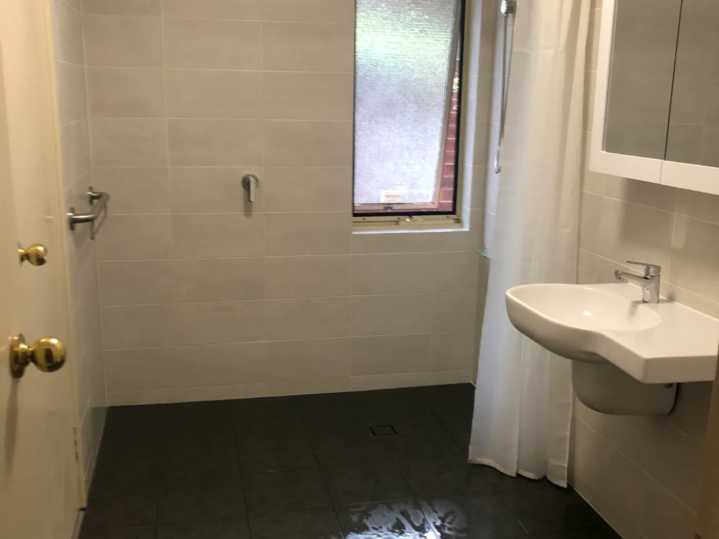 Finished accessible bathroom in a Perth home after conversion, with a level shower floor draining to a floor waste, a grab rail by the door and a wall-hung basin