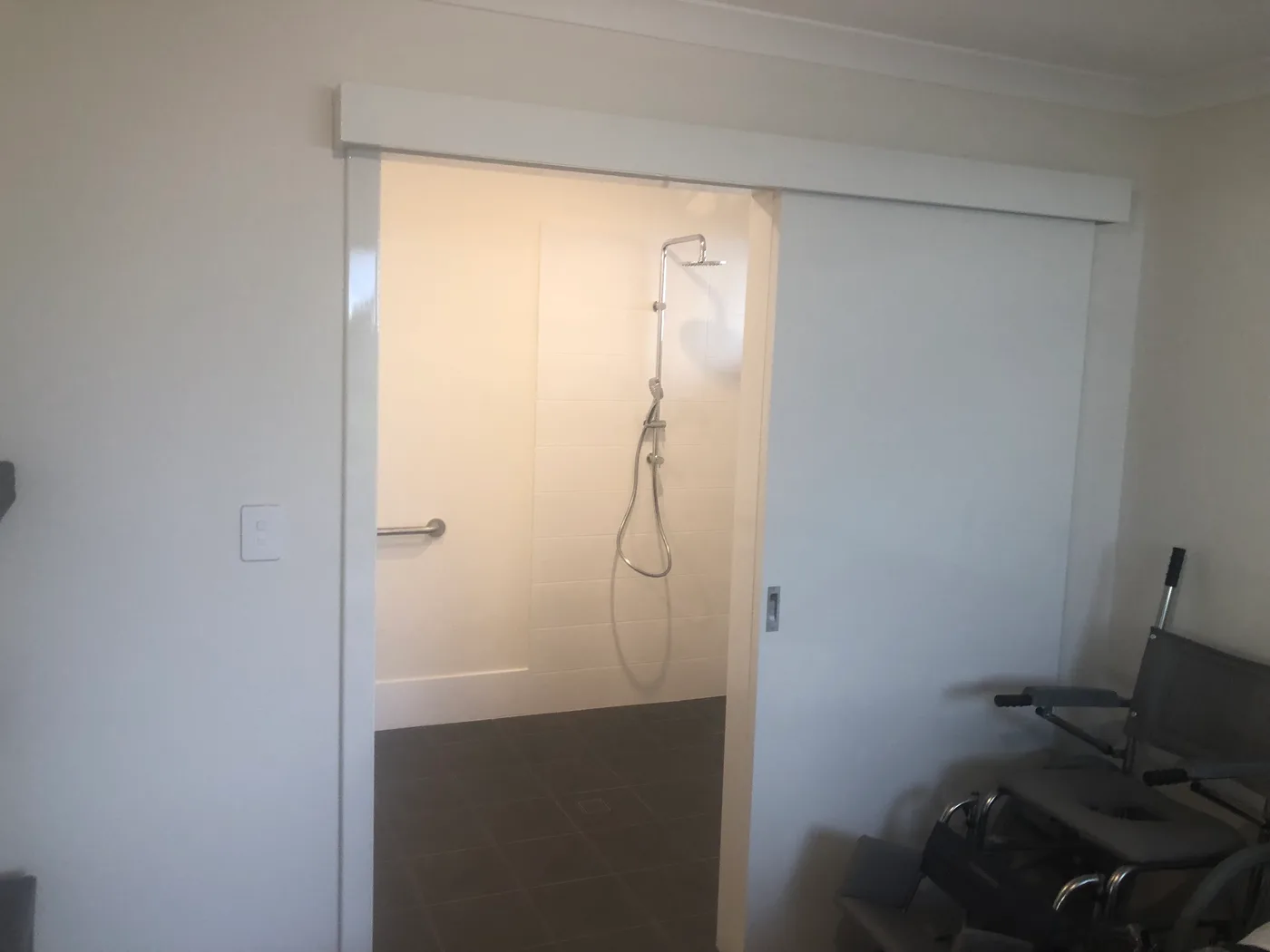 A widened bathroom doorway in a Perth home fitted with a cavity sliding door, wide enough for a wheelchair, with the shower and grab rail visible beyond
