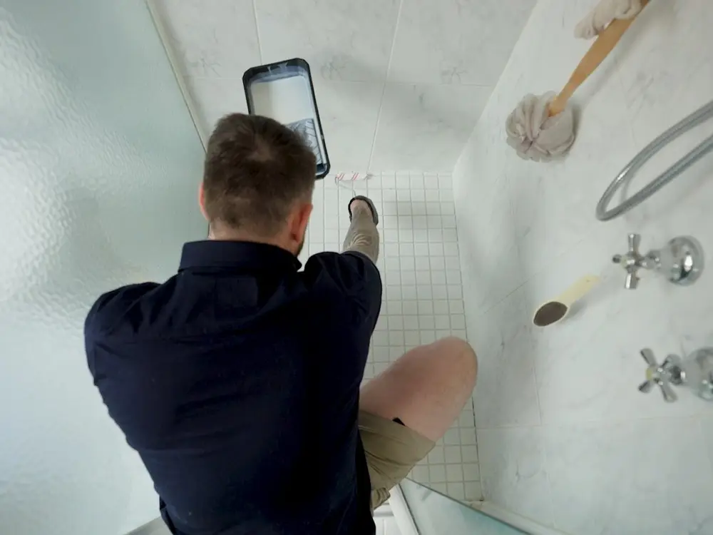 A clear non-slip coating being rolled onto a white tiled shower floor, seen from above