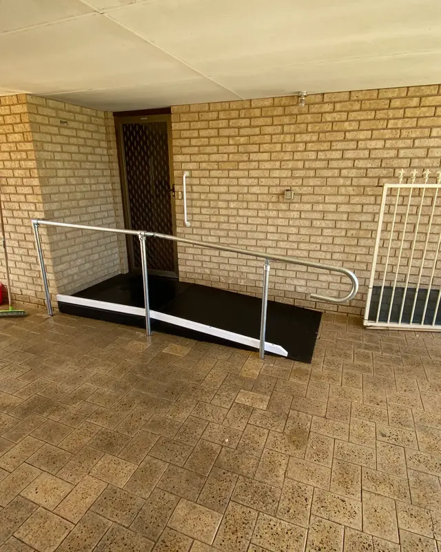 A ramp with a black non-slip surface and a galvanised steel handrail leading to a back door under a patio in Perth