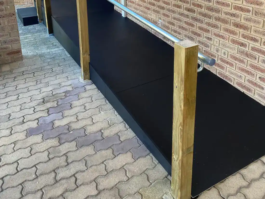 A non-slip wheelchair ramp running along the side of a Perth brick home to the front door, with timber posts and a galvanised handrail