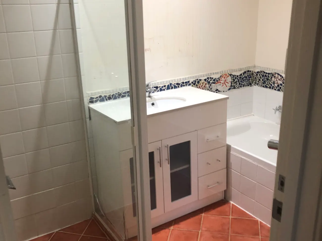 Before: a Perth bathroom with a framed shower screen stepping over a hob, terracotta floor tiles, a separate bath and a standard vanity